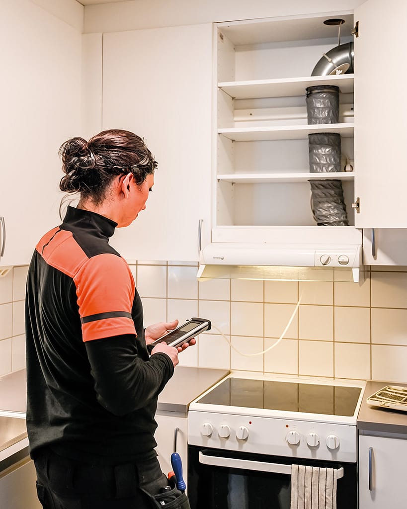 Kvinnlig ventilationstekniker utför OVK, obligatorisk ventilationskontroll, i ett kök